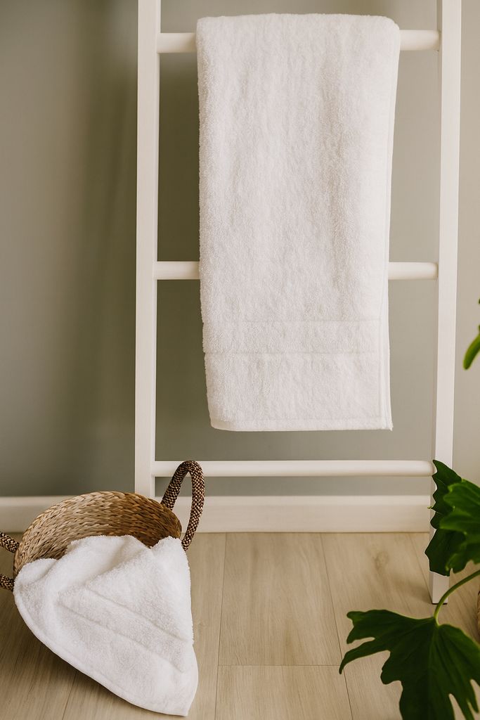 White towel hanging on a white towel rack against a neutral wall with a plant in the corner.