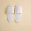 A pair of white towelling open-toe slippers placed on a neutral background.