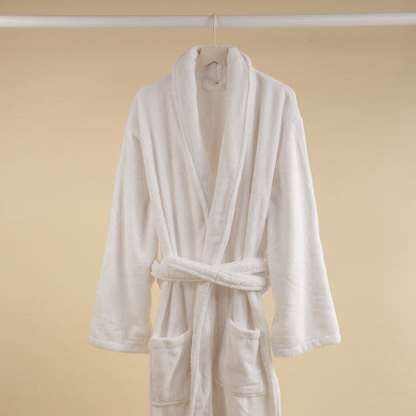 A white coral fleece bathrobe hanging on a rod against a beige background.