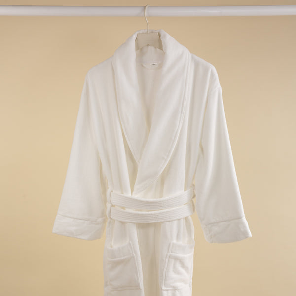 A white velour towelling bathrobe hanging against a beige background.