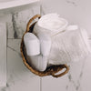 White slippers and folded towels in a woven basket on a marble floor.