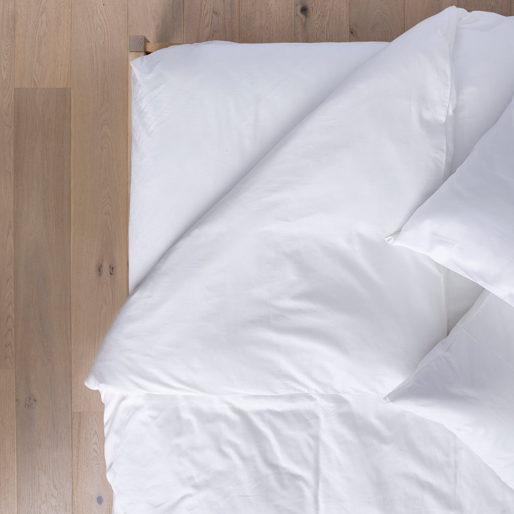 White comforter on a bed against a wooden headboard