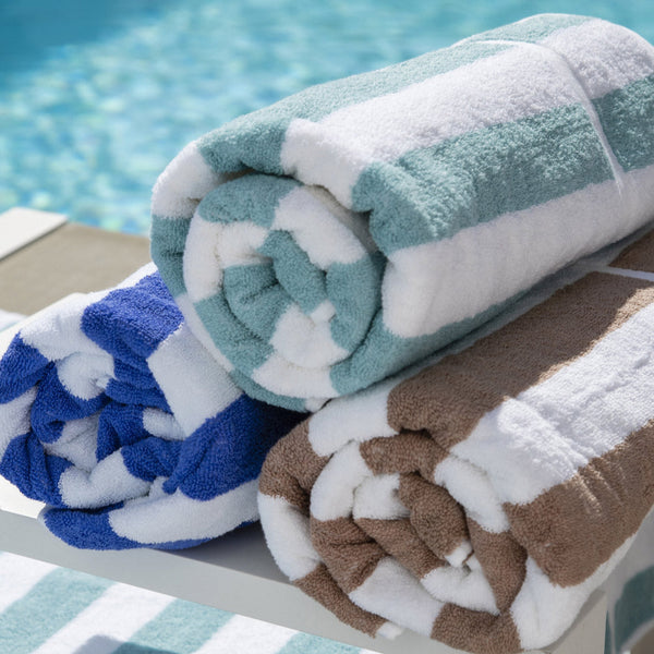 A collection of folded pool and beach towels in various colors, placed on a white rack by a poolside.
