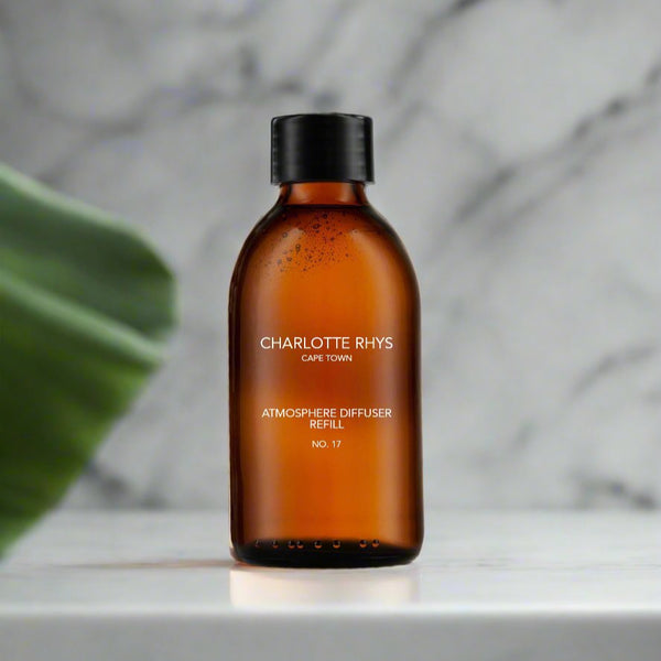 A brown glass bottle labeled 'charlotte rhys atmosphere diffuser refill' with a capacity of 1 litre, placed on a marble surface with a plant in the background.