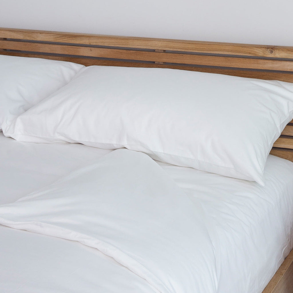A white duvet cover on a bed, with wooden headboard and a pillow visible on the bed.