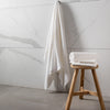 A set of white towels displayed on a wooden stool next to a marble-tiled wall in a bathroom setting.