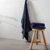 Navy blue towel draped over a wooden stool against a marble wall.