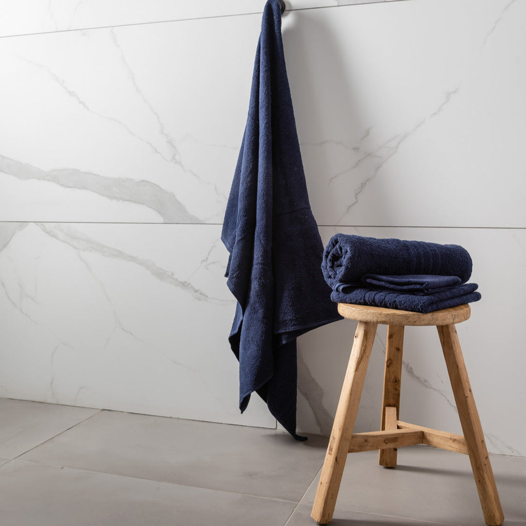 Navy blue towel draped over a wooden stool against a marble wall.