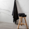 Black towels on a wooden stool against a marble wall.