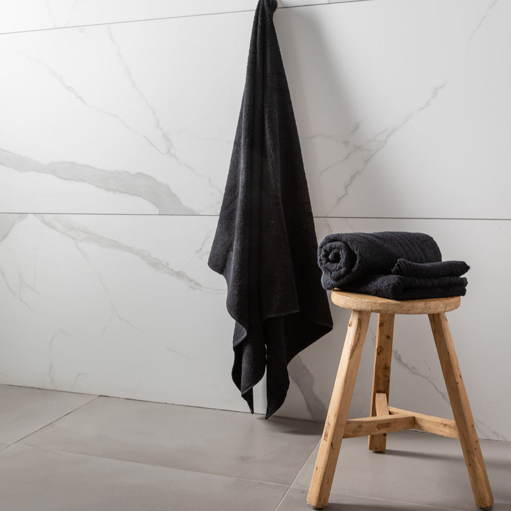 Black towels on a wooden stool against a marble wall.