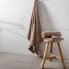 Brown towel hanging and folded on a wooden stool against a marble wall.