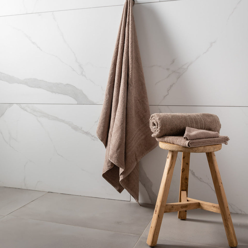 Brown towel hanging and folded on a wooden stool against a marble wall.